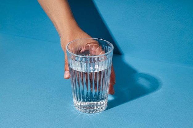 Mano femenina sosteniendo un vaso de agua sobre fondo azul.