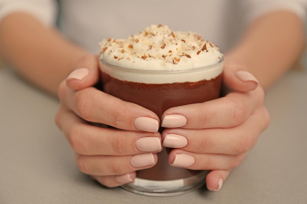 Mano femenina sosteniendo un vaso con mousse de chocolate en la mesa