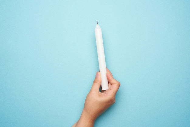 Mano femenina sosteniendo una vela de cera blanca sobre azul