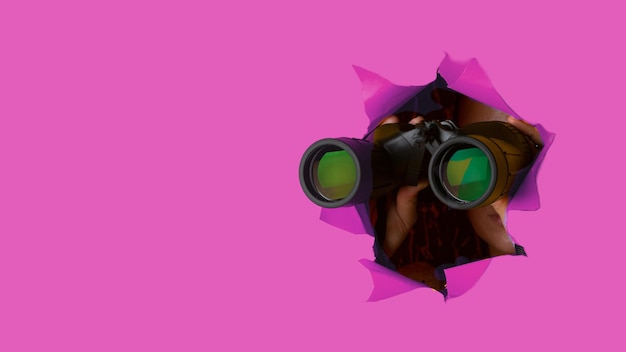 Mano femenina sostiene binoculares negros sobre un fondo rosa Concepto de búsqueda y búsqueda de viaje