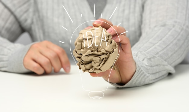 La mano femenina sostiene una bola de papel marrón arrugada. Nueva idea, lluvia de ideas