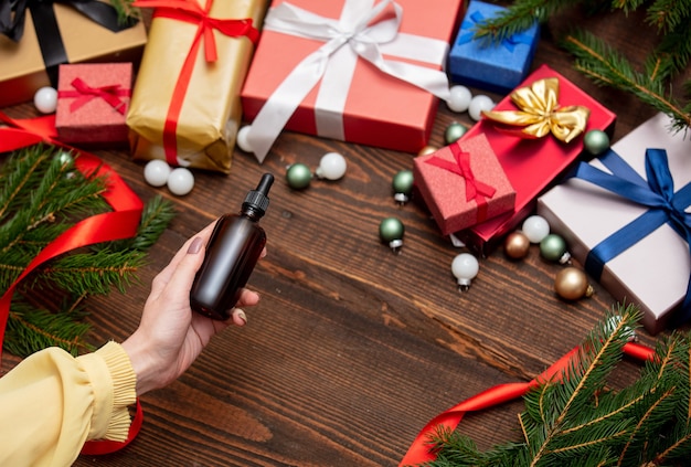 Mano femenina sostiene la botella de perfume cerca de los regalos de Navidad