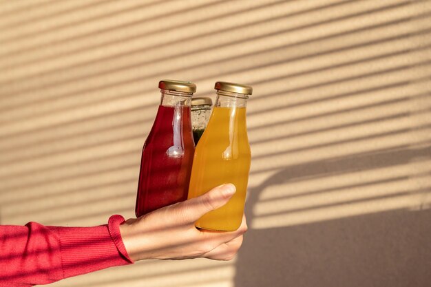 mano femenina sostiene botellas de vidrio con jugos o batidos multicolores