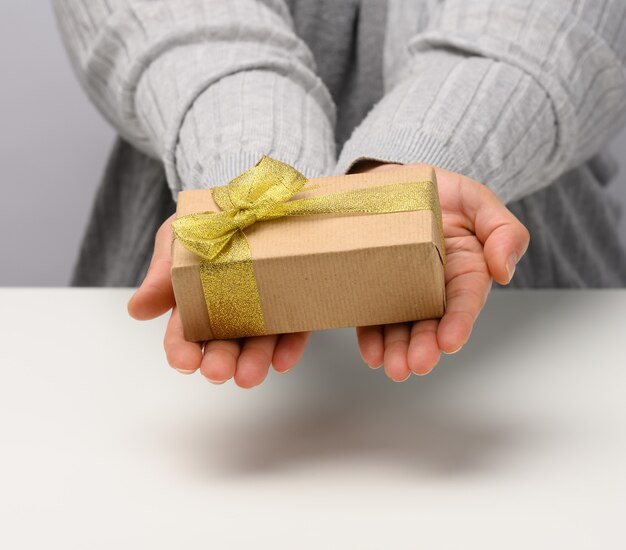 Mano femenina sostiene una caja de regalo sobre un fondo gris, concepto de feliz cumpleaños, cerrar