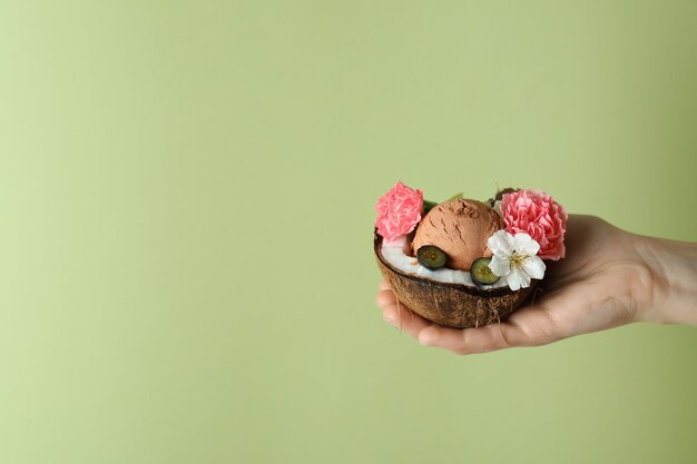 Mano femenina sostiene coco con helado de frutas sobre fondo verde