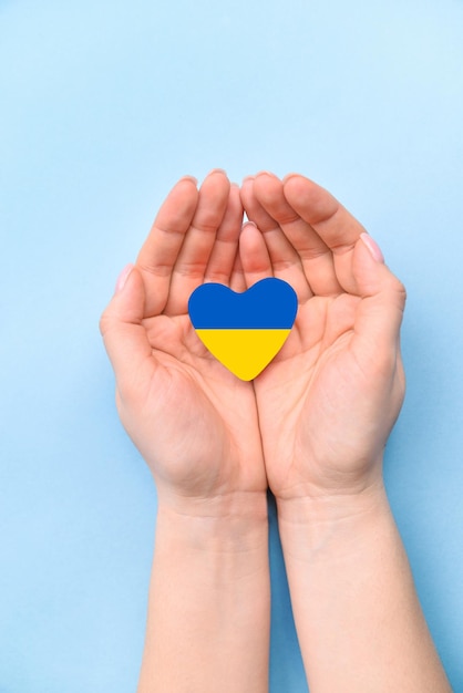 La mano femenina sostiene un corazón de una bandera ucraniana amarillo-azul sobre fondo azul. paren la guerra