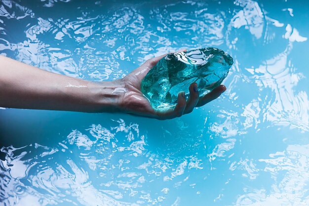 Foto una mano femenina sostiene un cristal turquesa sobre agua azul fondo de pantalla vertical