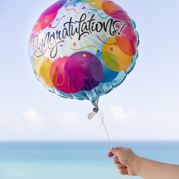 Foto una mano femenina sostiene un globo de colores con felicitaciones sobre un fondo de cielo azul