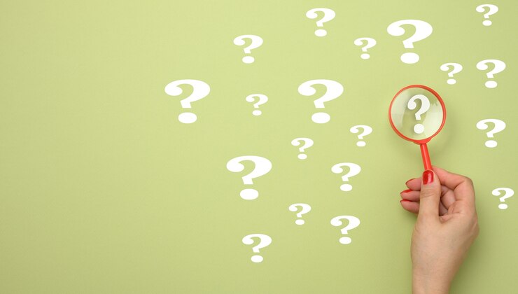 Foto mano femenina sostiene una lupa de plástico y signos de interrogación sobre un fondo verde. el concepto de encontrar una respuesta a las preguntas, la verdad y la incertidumbre.
