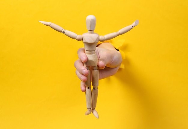 La mano femenina sostiene una marioneta de madera a través de un agujero rasgado papel amarillo Arte conceptual Minimalismo