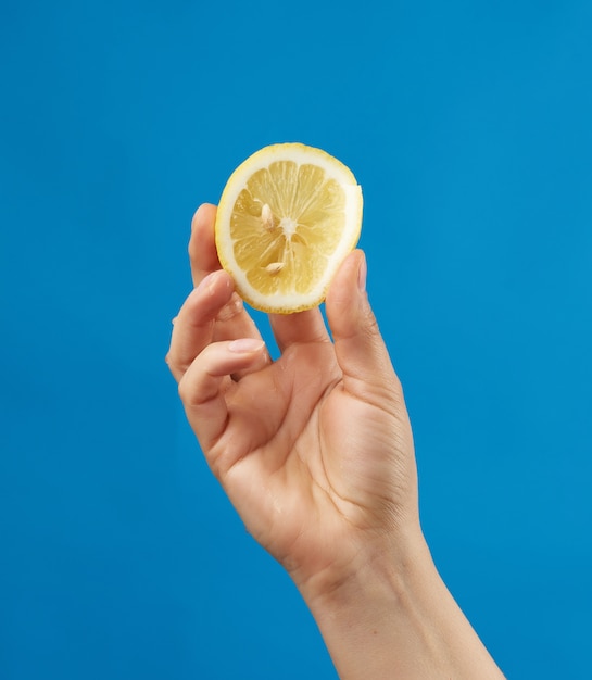 La mano femenina sostiene medio limón amarillo y lo aprieta