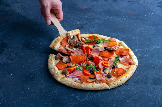 Mano femenina sostiene pizza con pala culinaria. Pizza de pepperoni recién preparada con salami y queso sobre un fondo oscuro. Almuerzo o cena tradicional italiana.