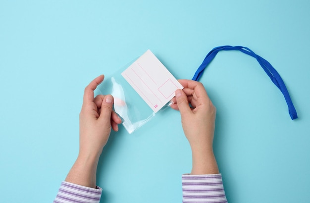 Mano femenina sostiene una placa de plástico transparente en un cordón azul sobre un fondo azul, vista superior