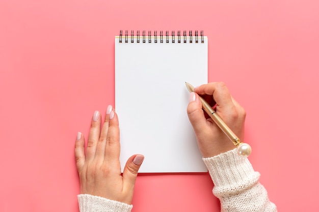 Mano femenina sostiene la pluma y escribe en el Bloc de notas blanco