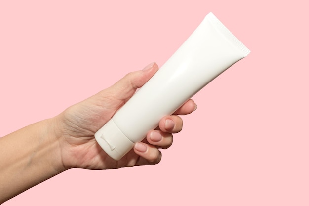 Una mano femenina sostiene un recipiente blanco para crema. Protección de la piel. Sobre un fondo rosa.