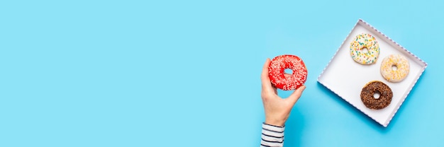 La mano femenina sostiene una rosquilla en un azul. Concepto de confitería, pastelería, cafetería.