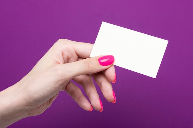 Mano femenina sostiene una tarjeta de presentación en blanco sobre un fondo púrpura.