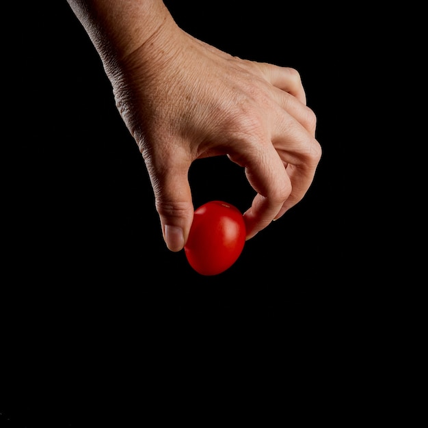 Mano femenina sostiene tomate cherry sobre un fondo negro