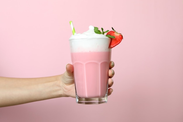 Mano femenina sostiene un vaso de batido de fresa sobre fondo rosa