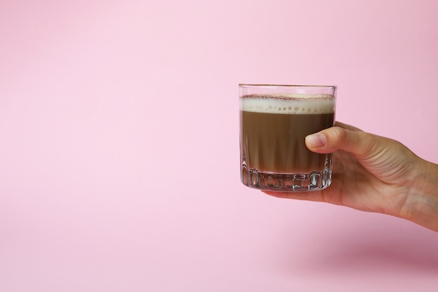 Mano femenina sostiene un vaso de café irlandés sobre fondo de color rosa