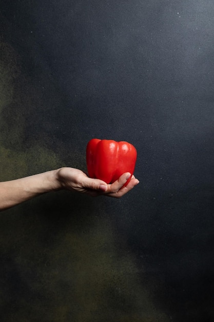 mano femenina sostiene verduras sobre un fondo oscuro