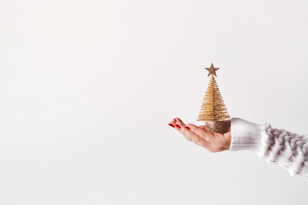 Mano femenina con suéter blanco sosteniendo un árbol de Navidad dorado con espacio de copia de estrellas