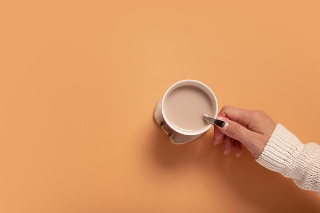 Mano femenina en suéter sosteniendo una taza de cacao en la vista superior de fondo de color con espacio de copia