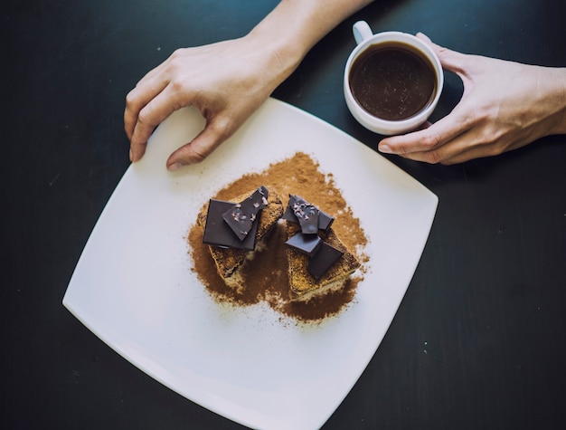 Mano femenina con una taza de café y un hermoso primer plano de pastel de chocolate sobre la mesa