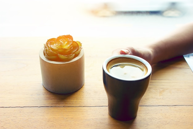 Mano femenina con una taza de café en la luz del sol de madera