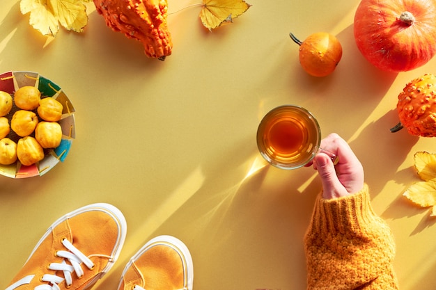 Mano femenina con taza de té, calabazas naranjas y plato de papel con membrillo, espacio de copia