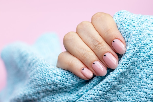 Mano femenina en una tela de suéter de punto azul con manicura