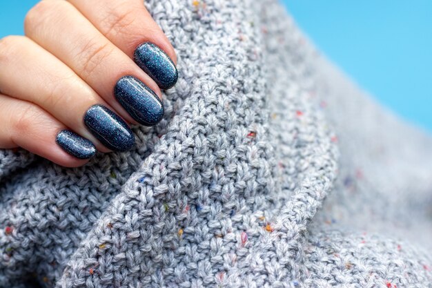 Mano femenina en una tela de suéter de punto gris con hermosa manicura