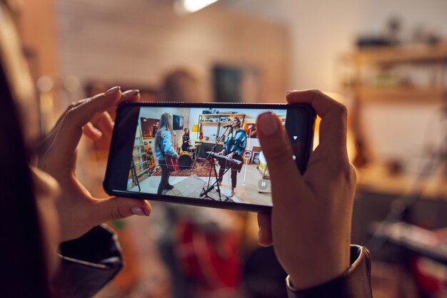 Mano femenina con teléfono inteligente durante la grabación de video de la interpretación musical