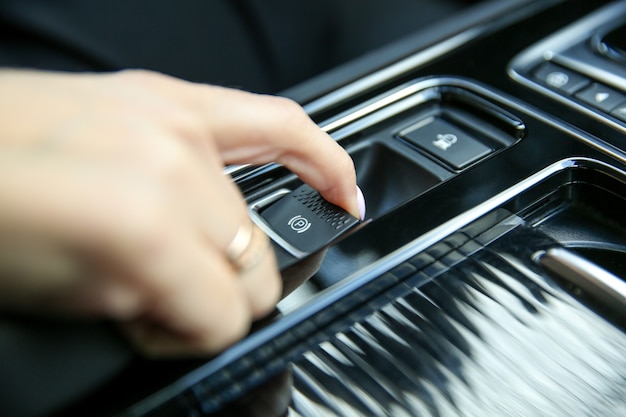 Mano femenina tira del botón del freno de mano en un coche moderno