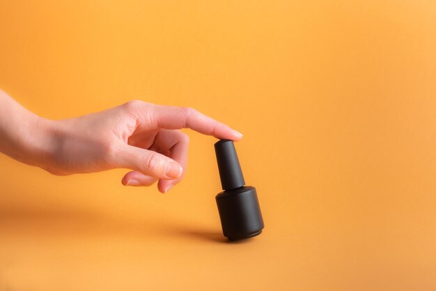 Mano femenina toca una botella de esmalte de uñas sobre un fondo naranja