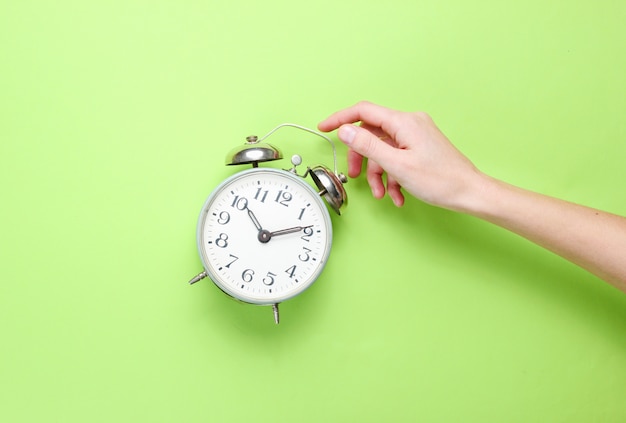 La mano femenina toma el despertador en fondo verde.