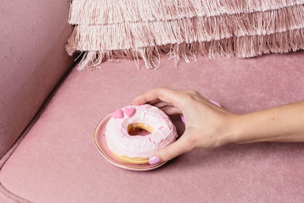 Mano femenina toma una rosquilla dulce rosa sobre una superficie rosa