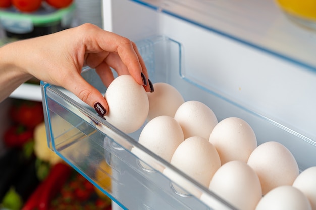 Mano femenina tomando huevos de una nevera