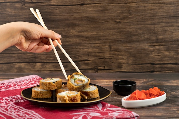 Mano femenina tomando sushi caliente con palillos en la superficie de madera.