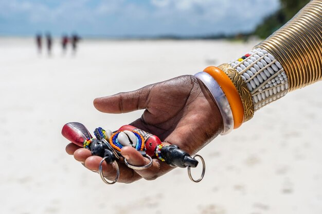 La mano femenina tribal Masai con una pulsera colorida tiene recuerdos a la venta para los turistas en la isla de Zanzíbar, Tanzania, África Concepto de viajes y vacaciones