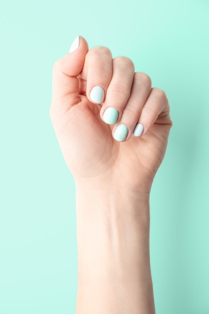 Mano femenina con uñas bien cuidadas y pintadas sobre un fondo verde