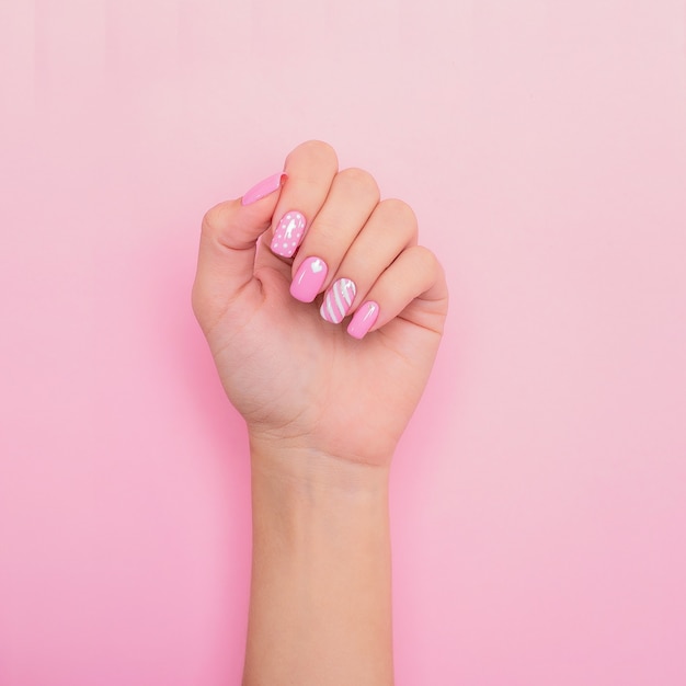 Mano femenina con uñas de manicura rosa, diseño de corazones