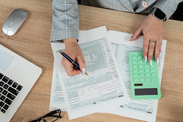 Mano femenina usando calculadora para llenar el formulario de impuestos 1040 ingresos individuales de negocios en la oficina