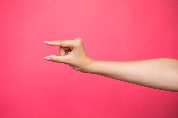 Mano femenina vacía fingiendo sostener algo, aislado sobre fondo de color rosa