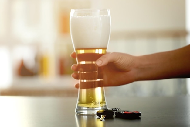 Mano femenina con vaso de cerveza y llave del auto en la mesa No beba y conduzca el concepto