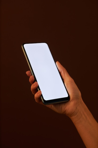 Mano femenina vertical que sostiene el teléfono inteligente con maqueta de pantalla blanca