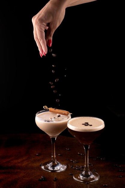 Mano femenina vertiendo granos de café tostados en un cóctel de martini espresso y baileys en vasos estriados y canela en primer plano