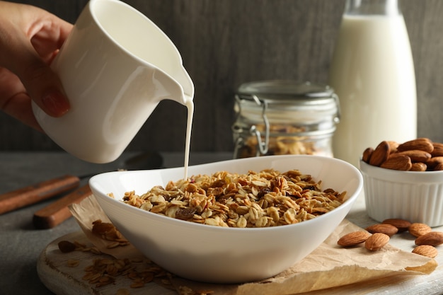 Mano femenina vierte la leche en un tazón con granola