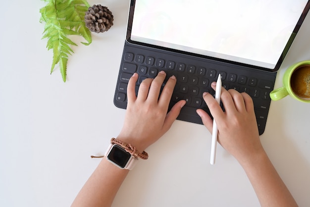 Mano femenina de la visión superior que mecanografía la tableta elegante del teclado en lugar de trabajo del estudio