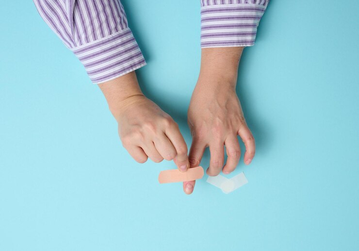 Foto mano femenina y yeso adhesivo médico marrón para el tratamiento de lesiones y cortes en la piel, fondo azul